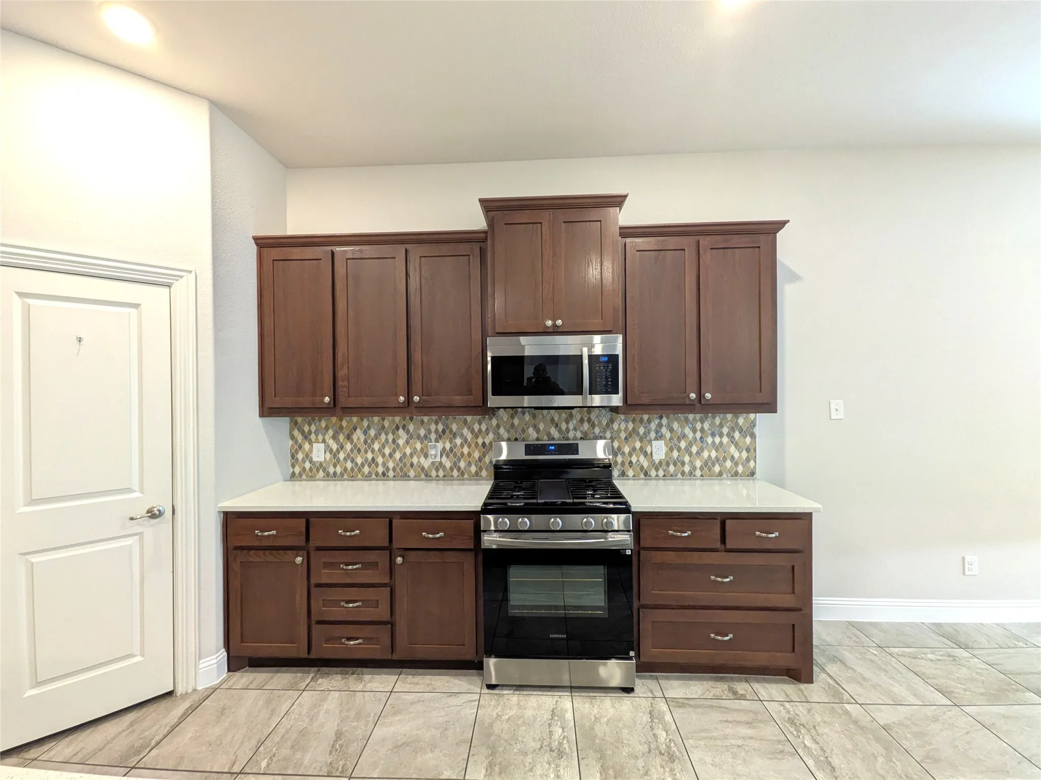 Full kitchen featuring wood cabinetry, stainless steel appliances, mosaic tile backsplash, white countertops, and tile flooring