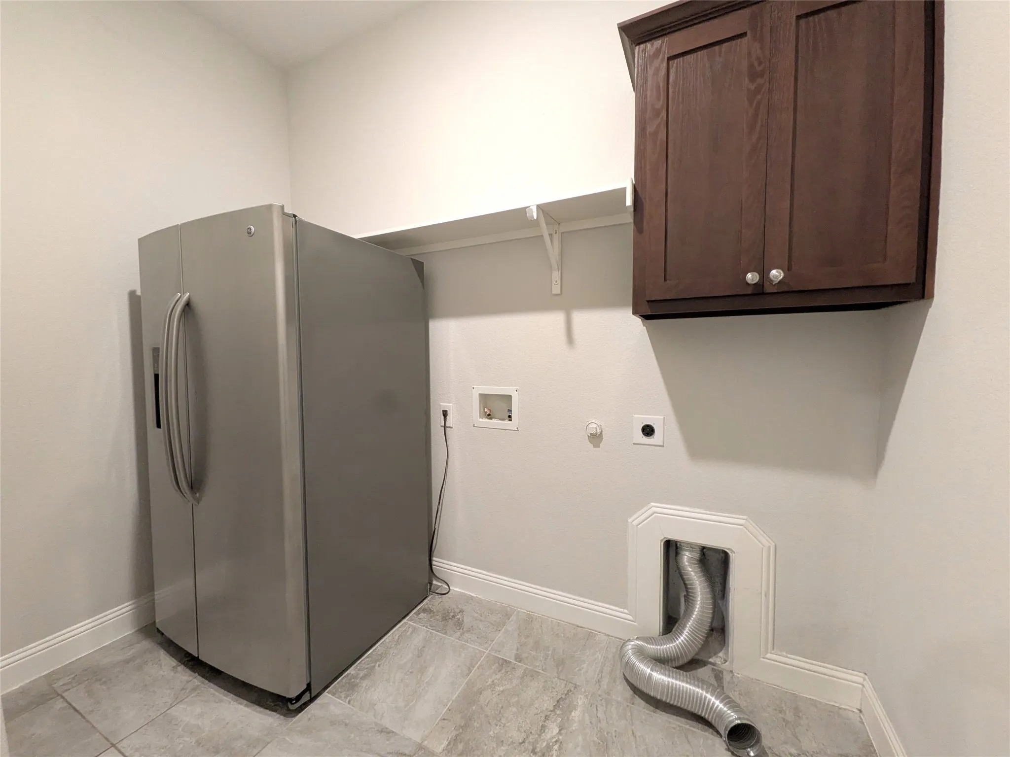 Laundry room featuring gray tile flooring, white walls, and a dark wood-finish wall cabinet
