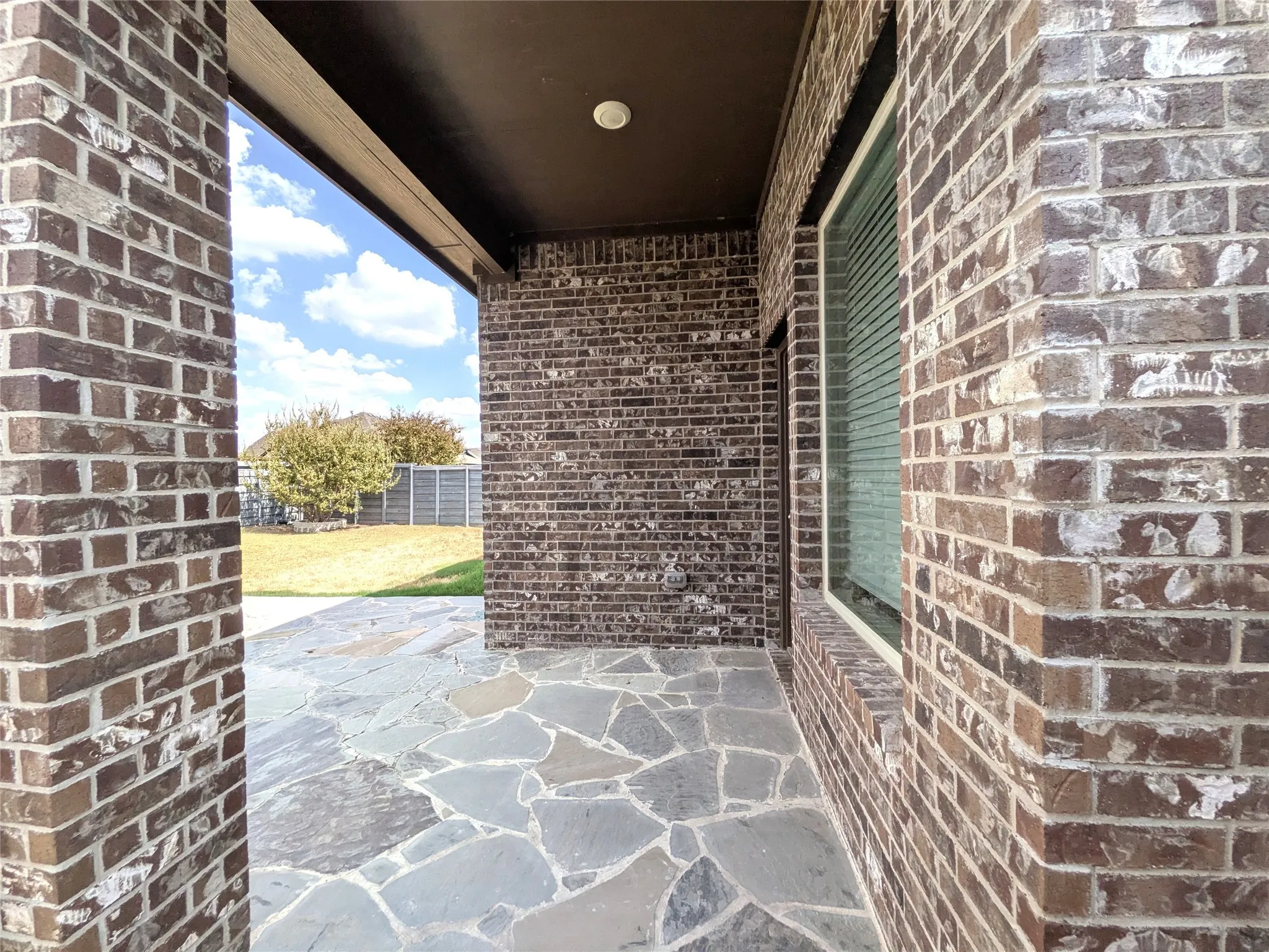 Covered patio with flagstone flooring, brick exterior, and a manicured lawn