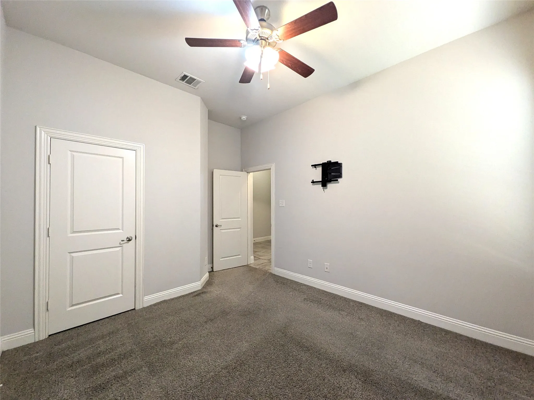 Textured carpet flooring, white interior doors, ceiling-mounted fan with integrated lighting, and a wall-mounted bracket