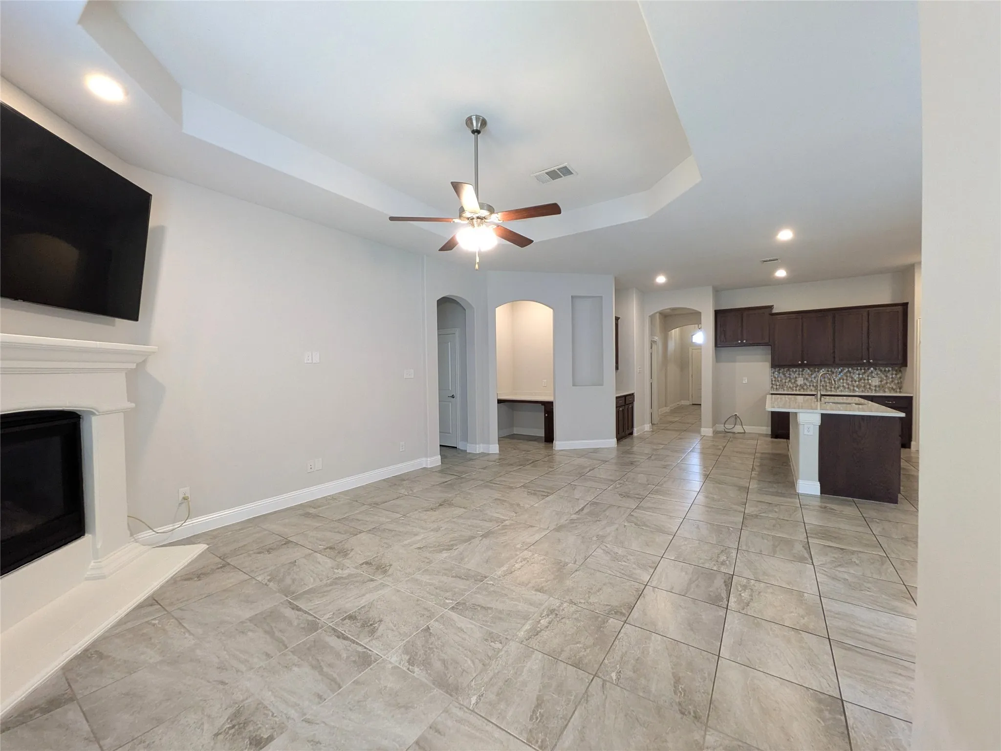 Tray ceiling with recessed lighting and ceiling fan, tiled flooring, white fireplace mantel, dark wood-finish cabinetry, and built-in desk area