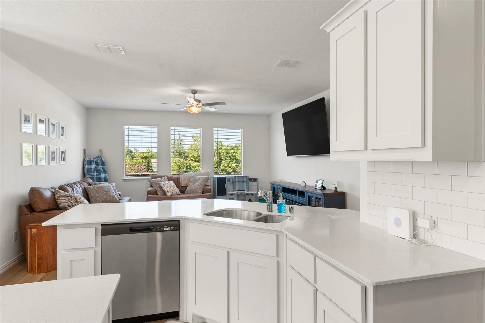 Kitchen island with an undermount sink, stainless steel dishwasher, white cabinetry, and light-colored countertops