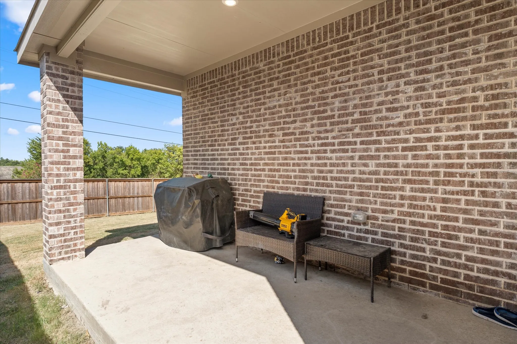 Covered concrete patio with brick support columns, brick exterior wall, and integrated ceiling lighting