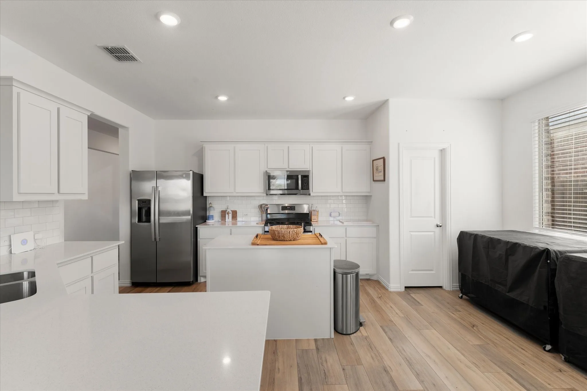 Modern kitchen featuring white cabinetry, light-toned wood-finish flooring, recessed lighting, and stainless steel appliances