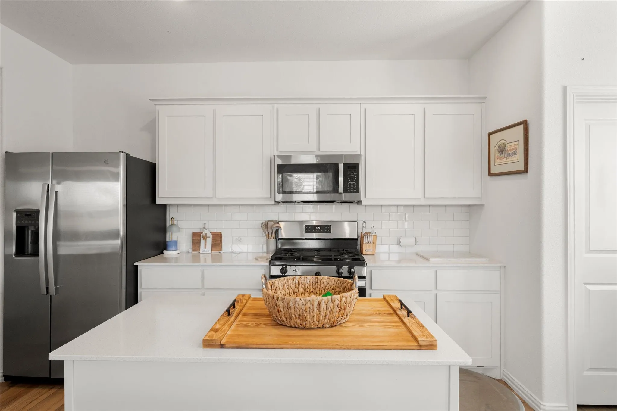 White shaker cabinetry, subway tile backsplash, stainless steel appliances, central island, and wood-finish flooring