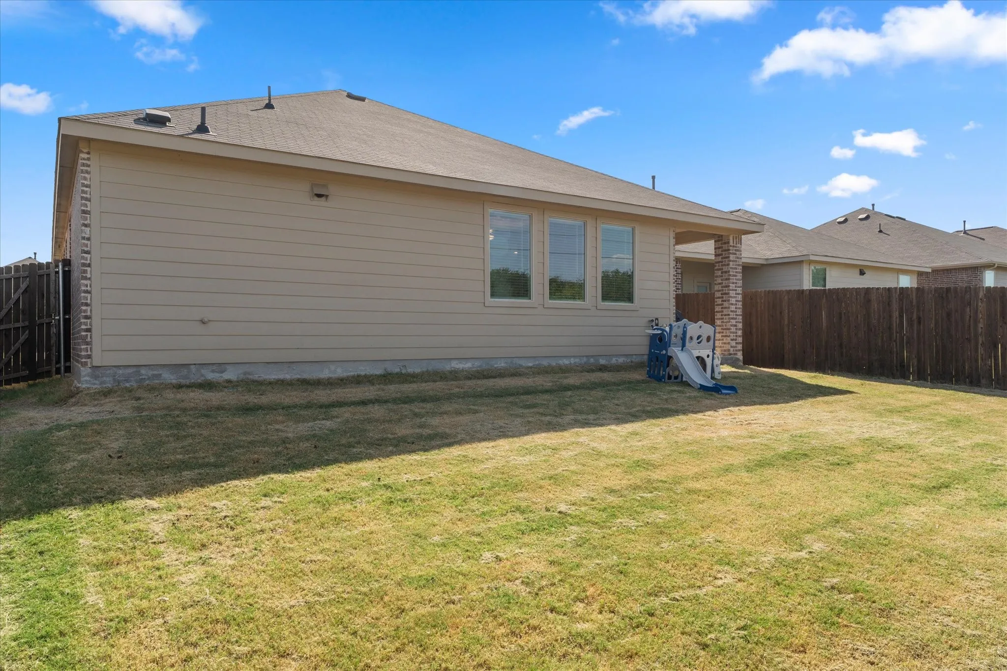 Expansive backyard featuring a privacy fence, covered patio, and triple-pane windows