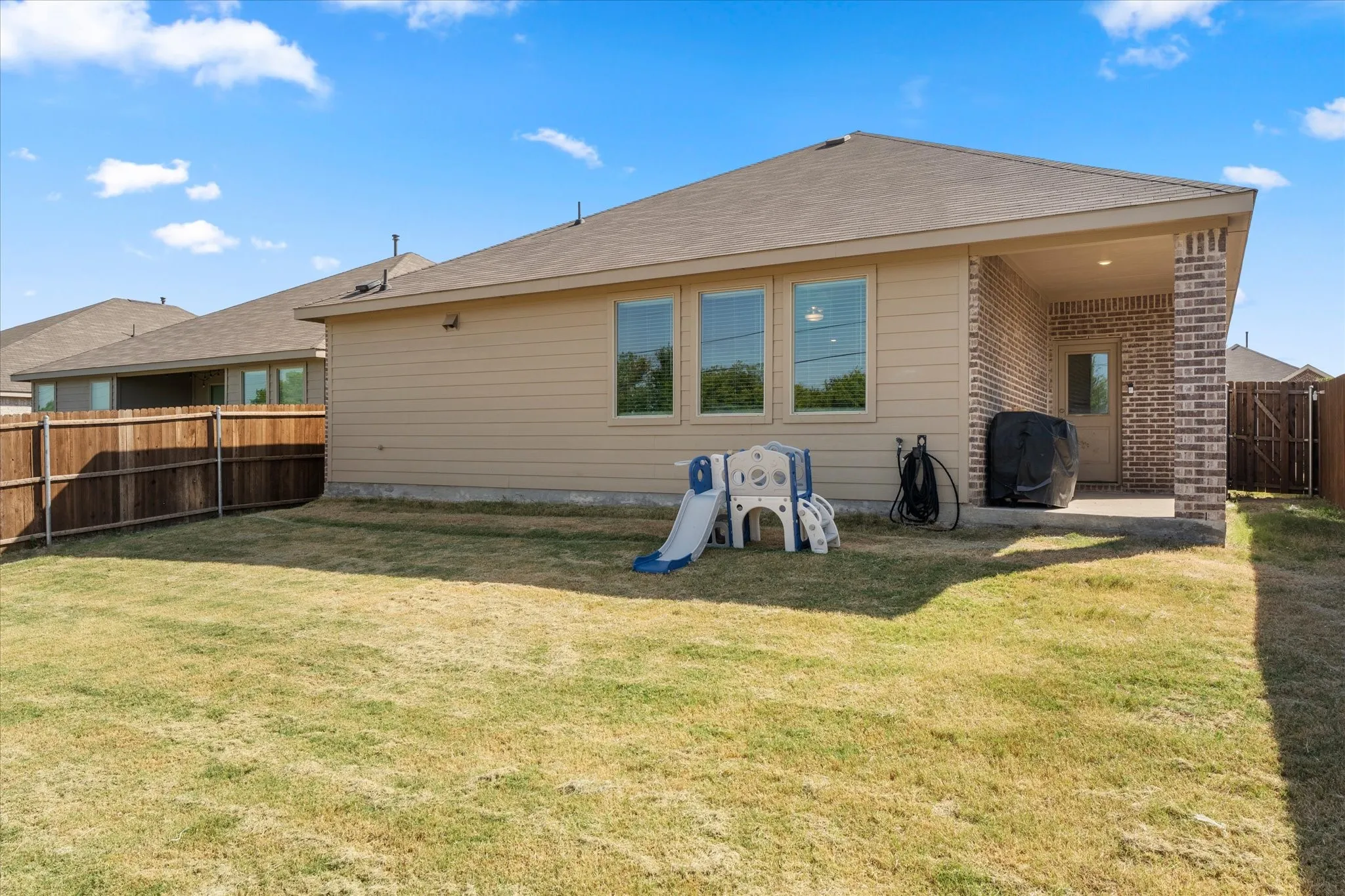 Expansive backyard with a covered patio featuring brick columns and a full privacy fence