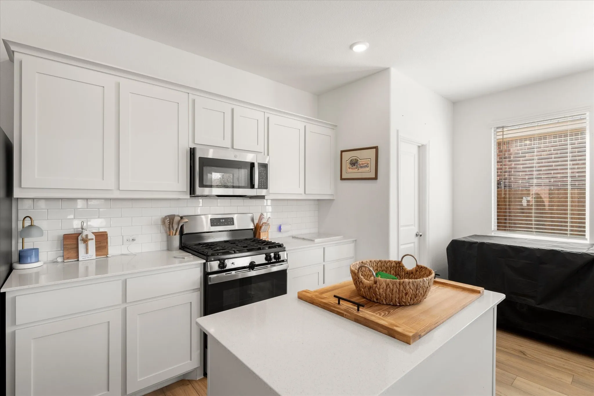 White cabinetry, subway tile backsplash, stainless steel appliances, quartz countertops, and wood-finish flooring