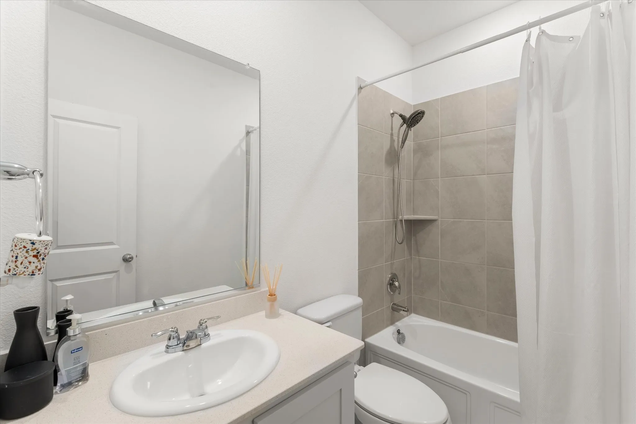 Bathroom featuring a vanity with an undermount sink, a large wall-mounted mirror, a toilet, and a shower-tub combination with tiled surround and shower head