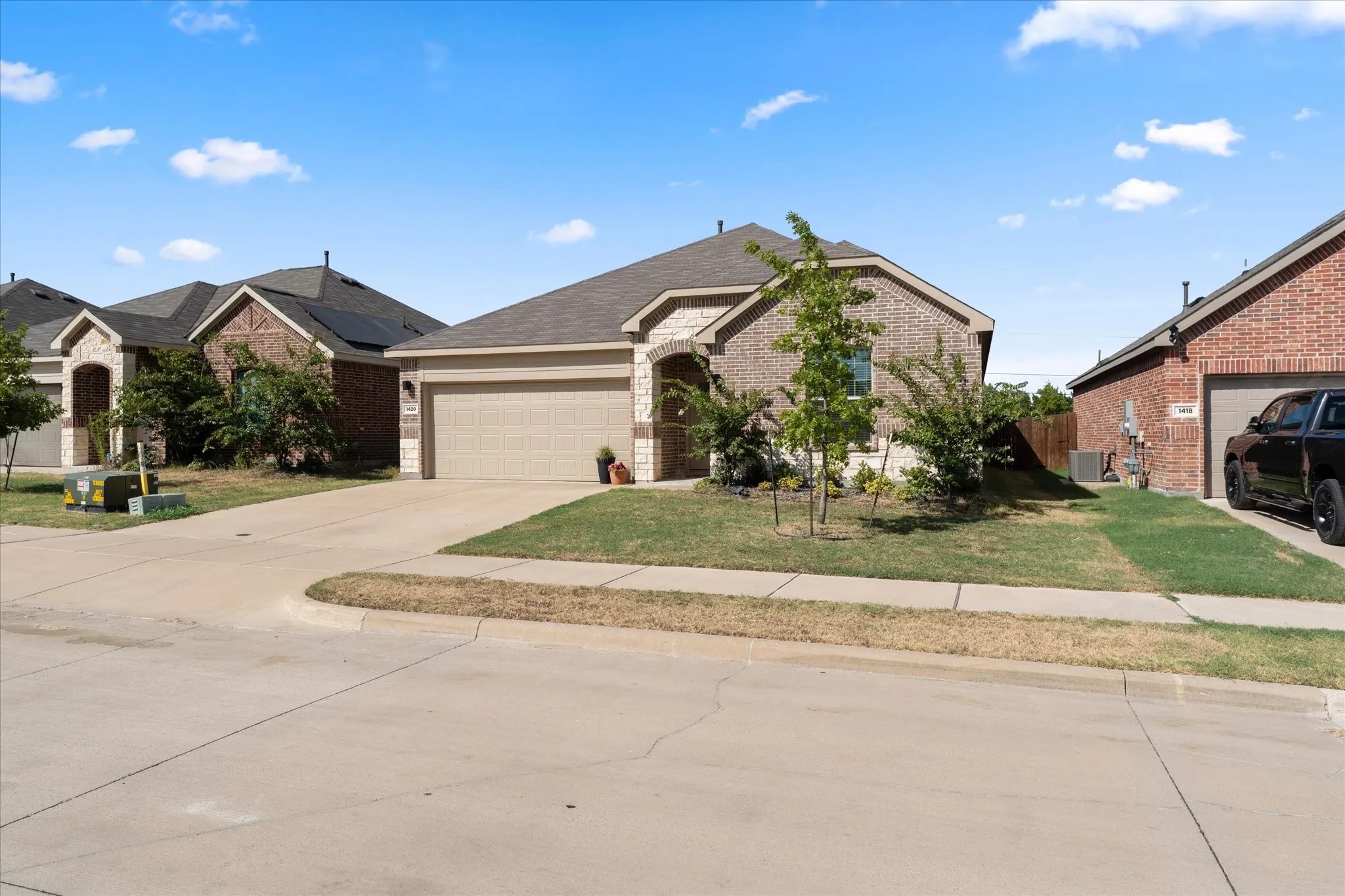 Brick and stone exterior, two-car garage, concrete driveway, front yard landscaping, and gabled roofline