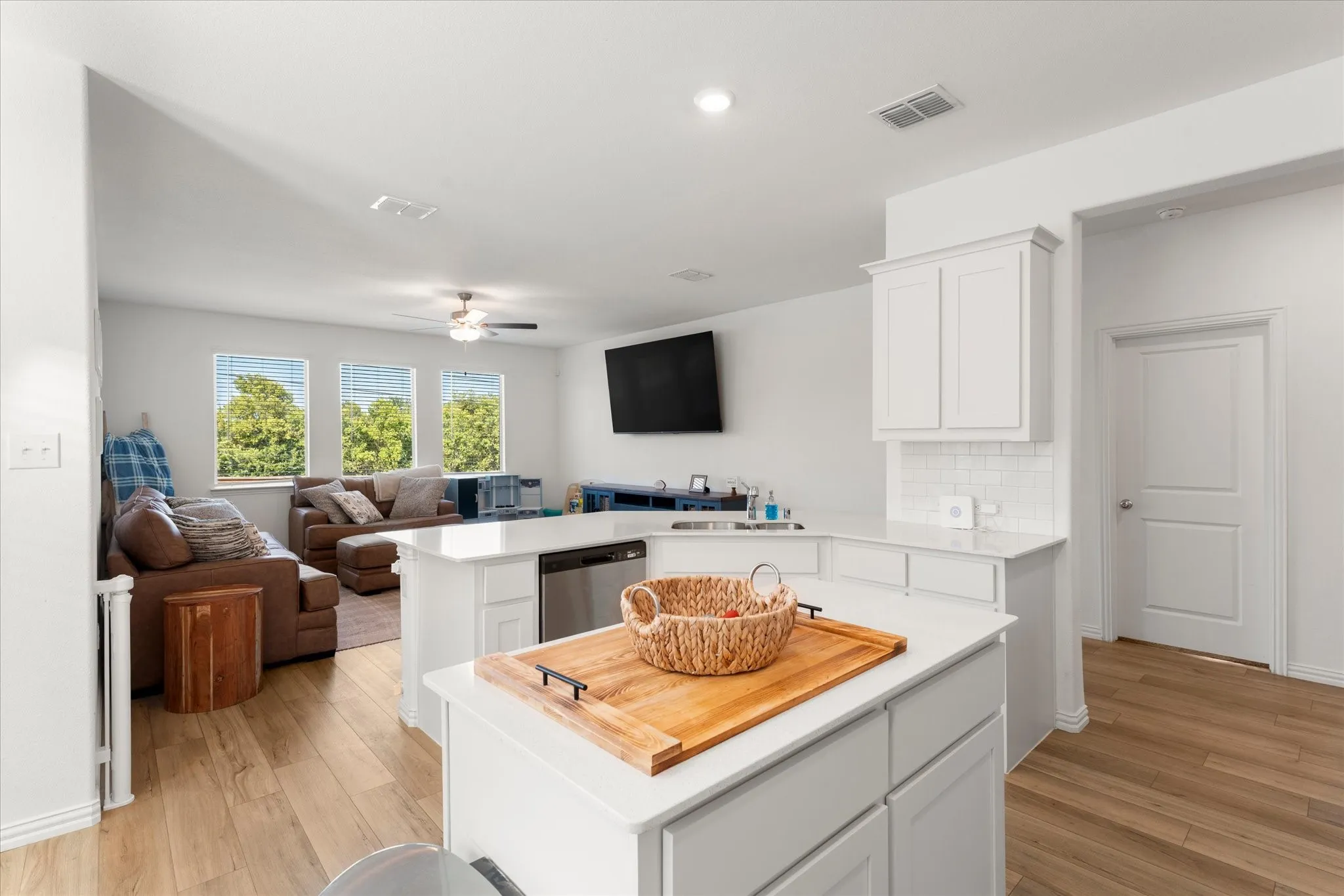 Open-concept layout with wood-finish flooring, white cabinetry, and light-toned countertops