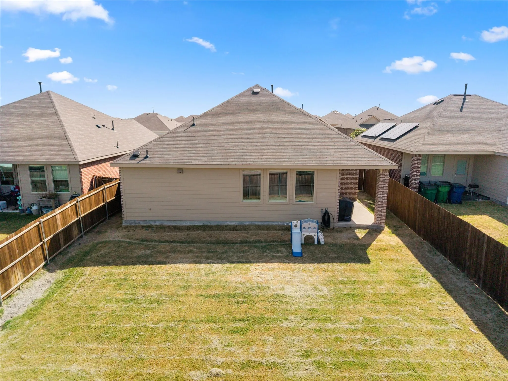 Expansive backyard featuring a manicured lawn, wood fencing, and a concrete patio