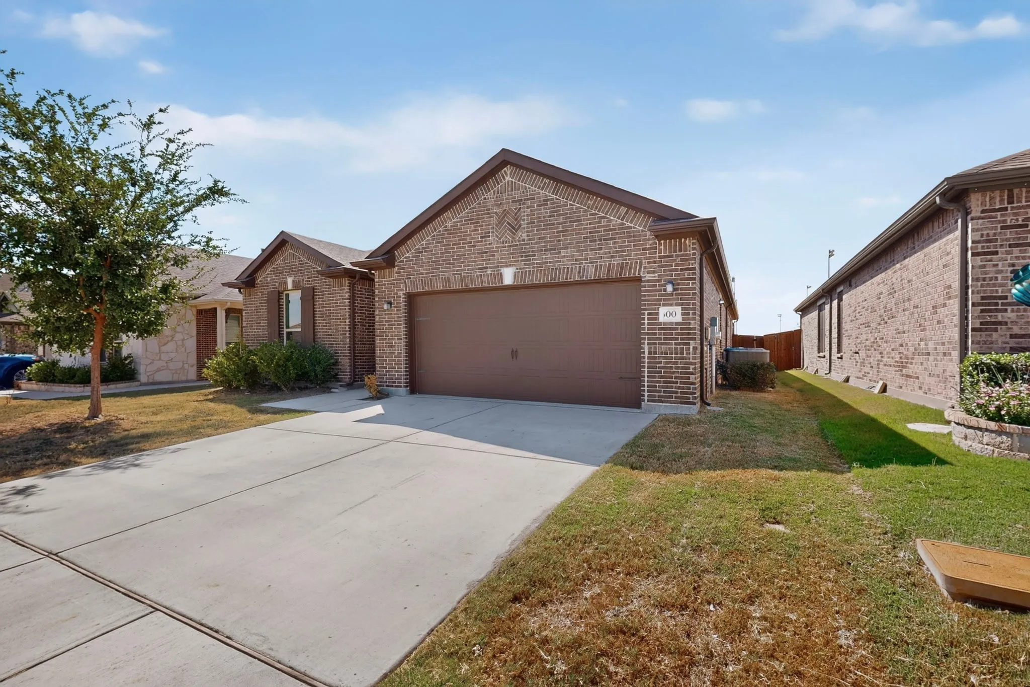 Brick exterior with a brown garage door, concrete driveway, and established landscaping