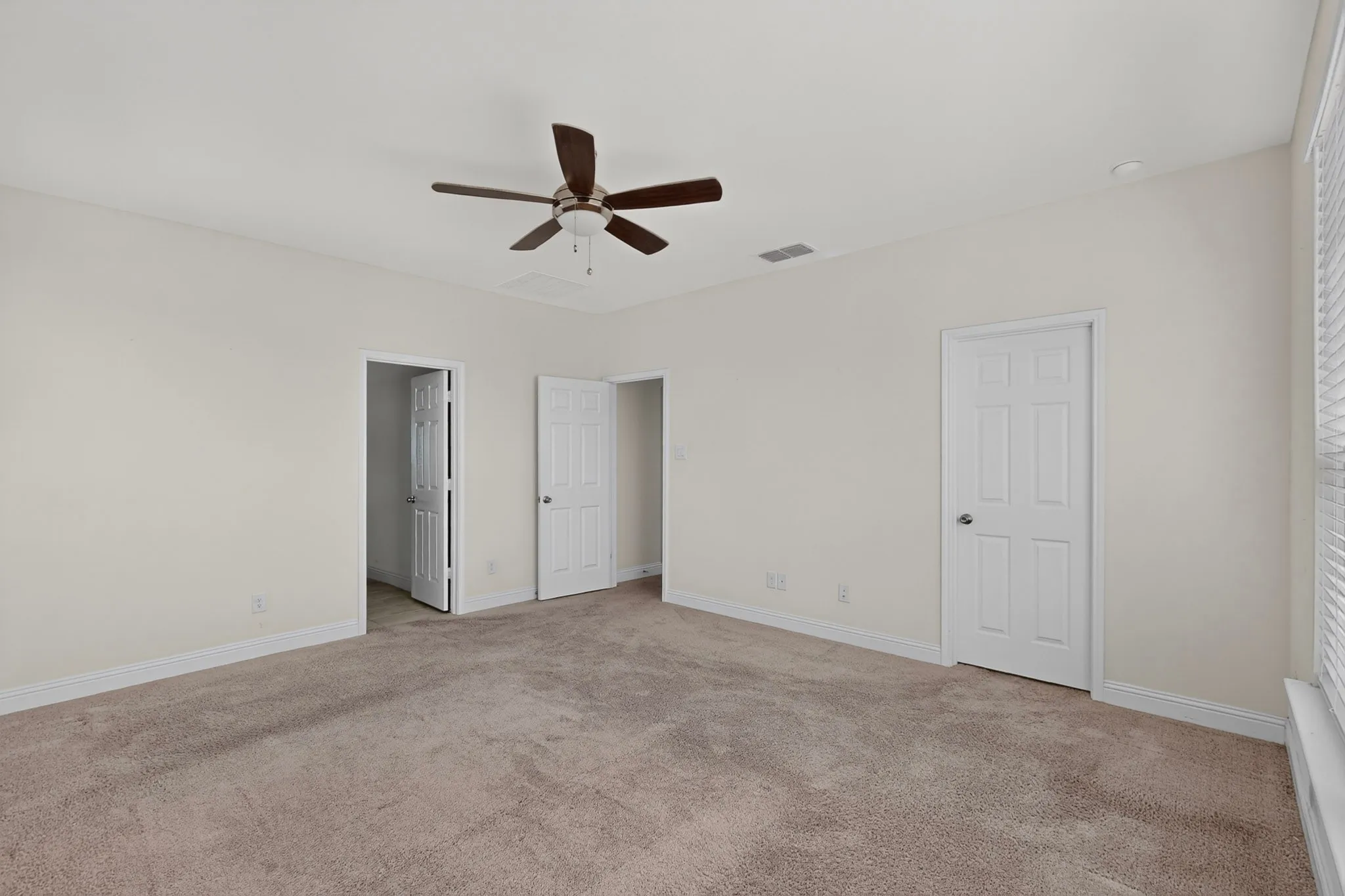 Spacious room featuring neutral carpeting, light-toned walls, and a ceiling fan with integrated lighting