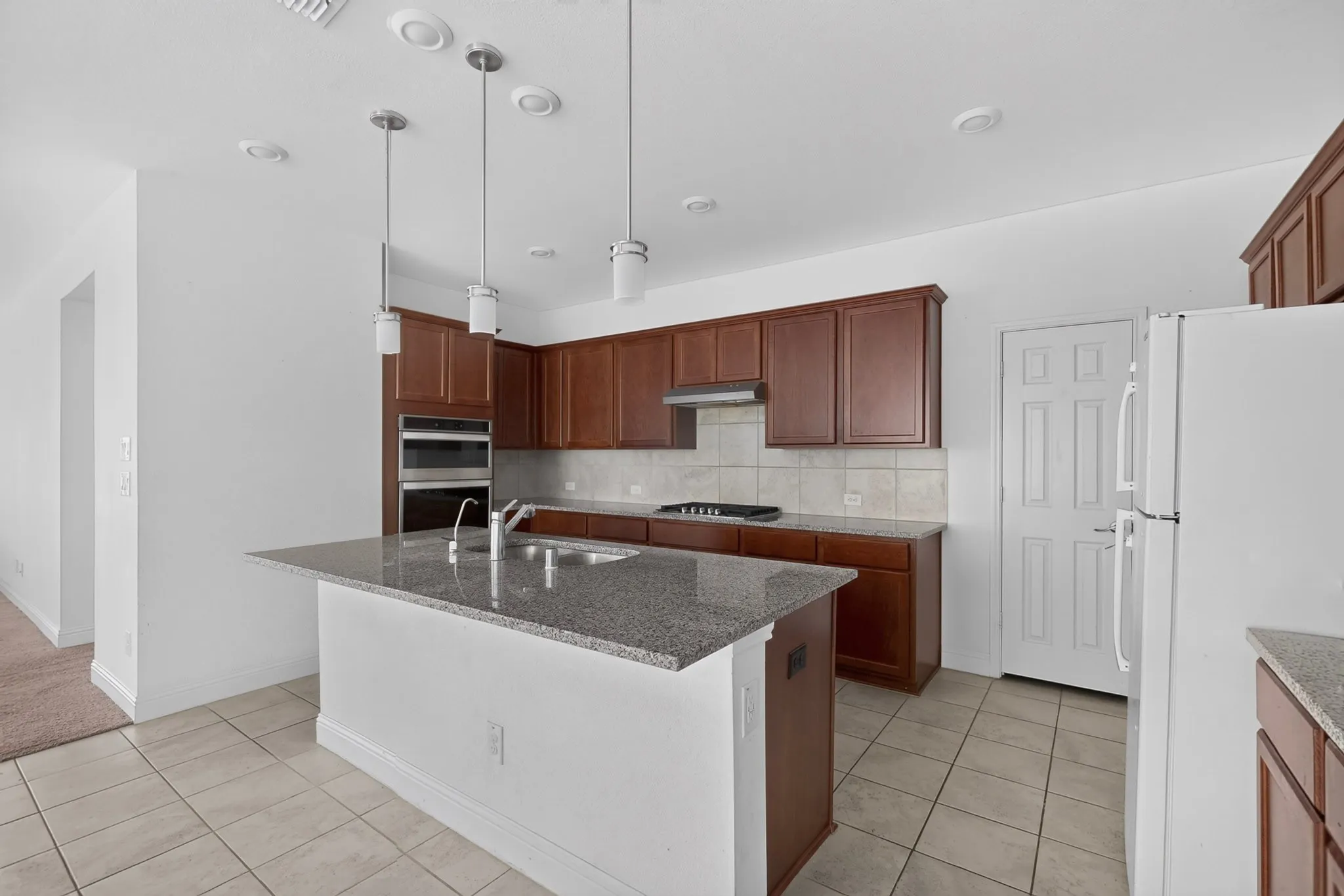 Kitchen featuring an island with a sink, pendant lighting, built-in ovens, and tile flooring