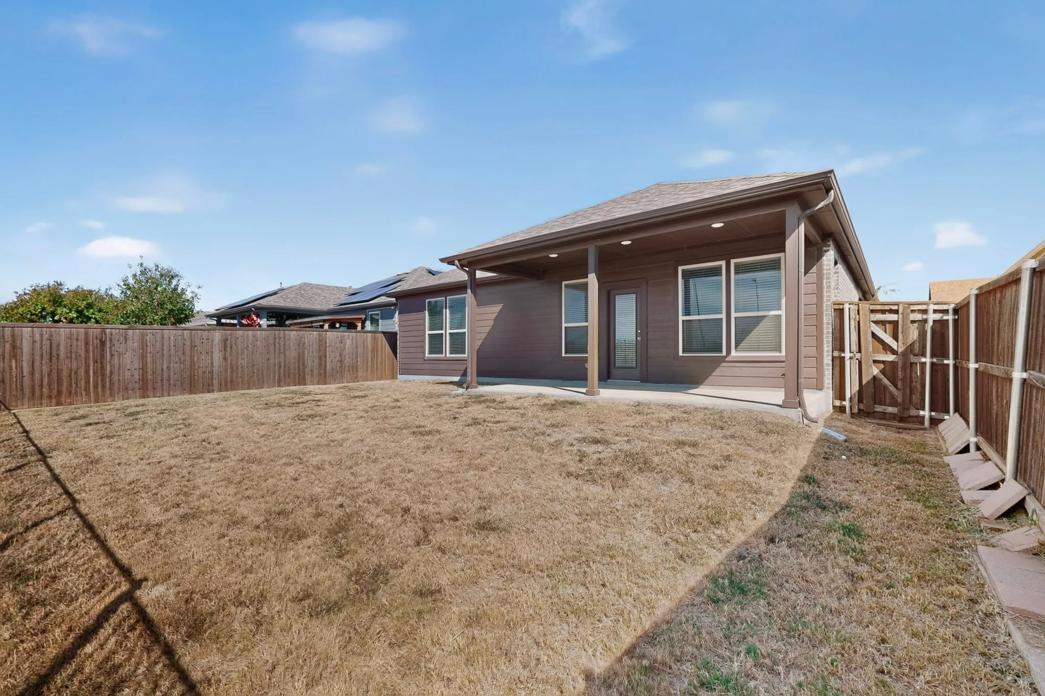 Expansive backyard with a covered patio, privacy fencing, and a wooden gate
