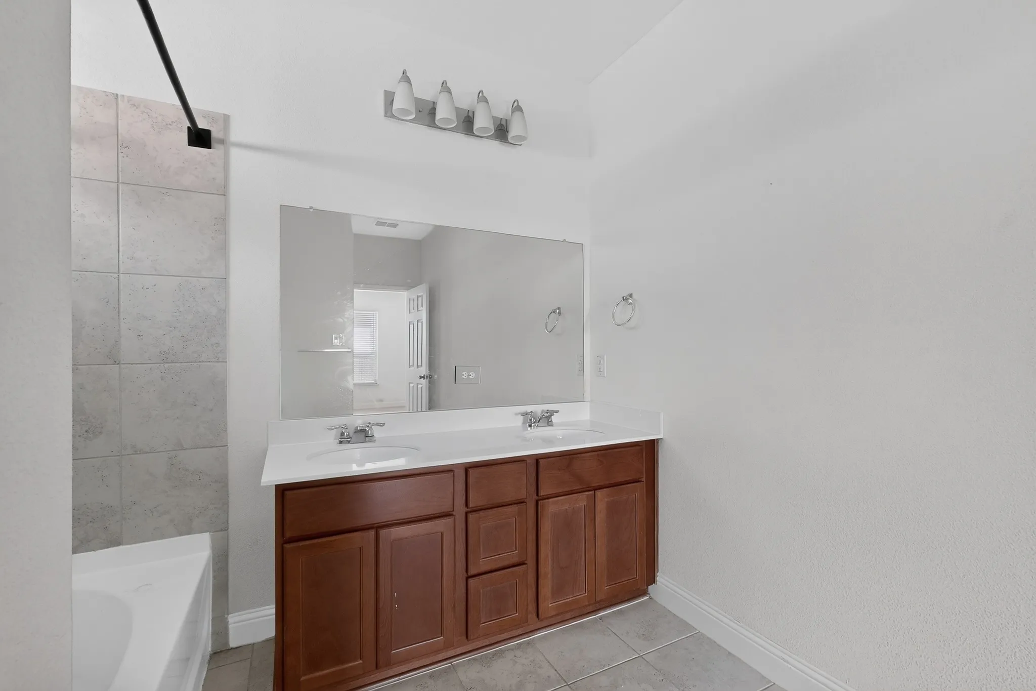 Double vanity with white countertops, integrated sinks, large wall mirror, and a four-light fixture