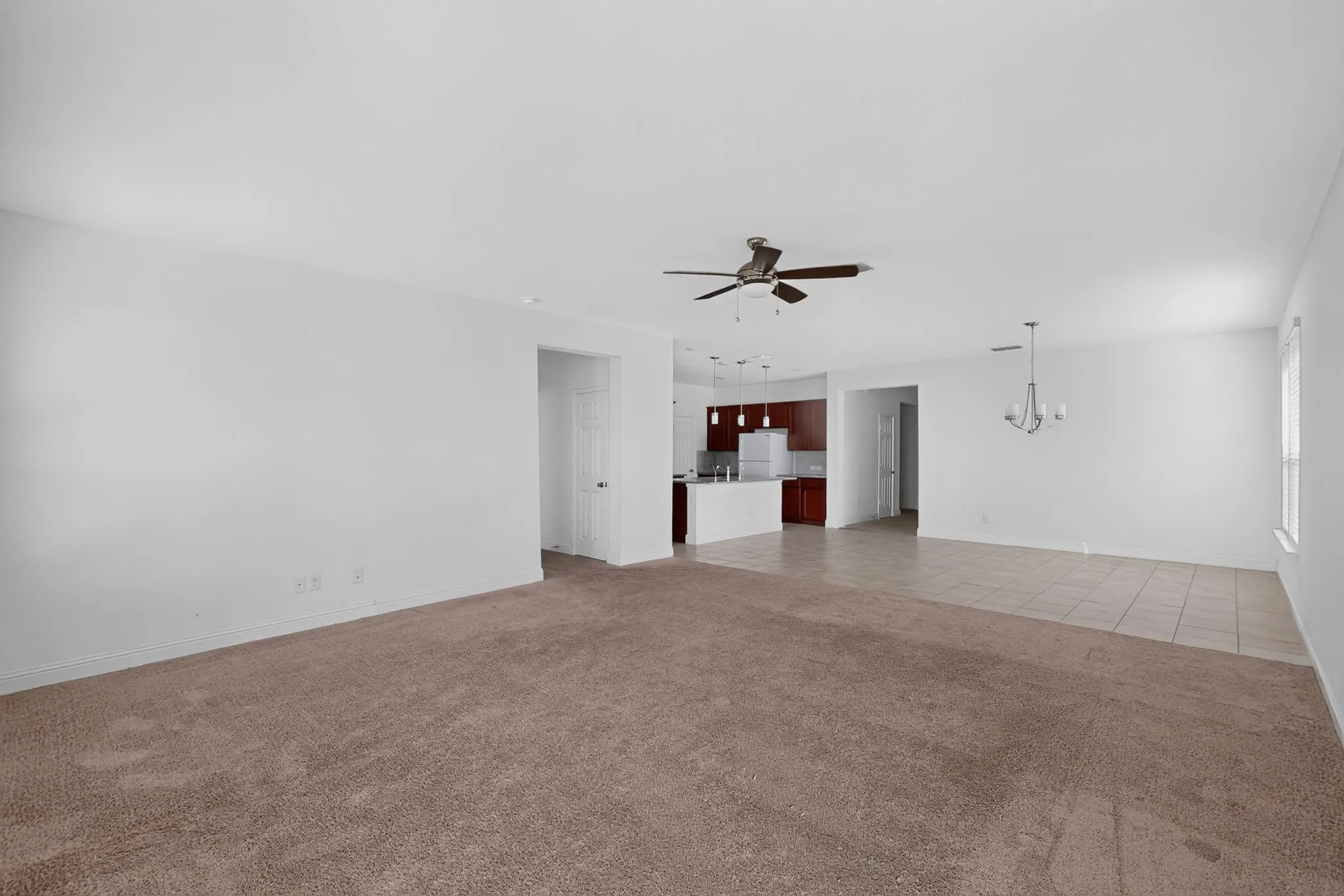 Expansive living area featuring carpet and tile flooring, a ceiling fan, and a chandelier
