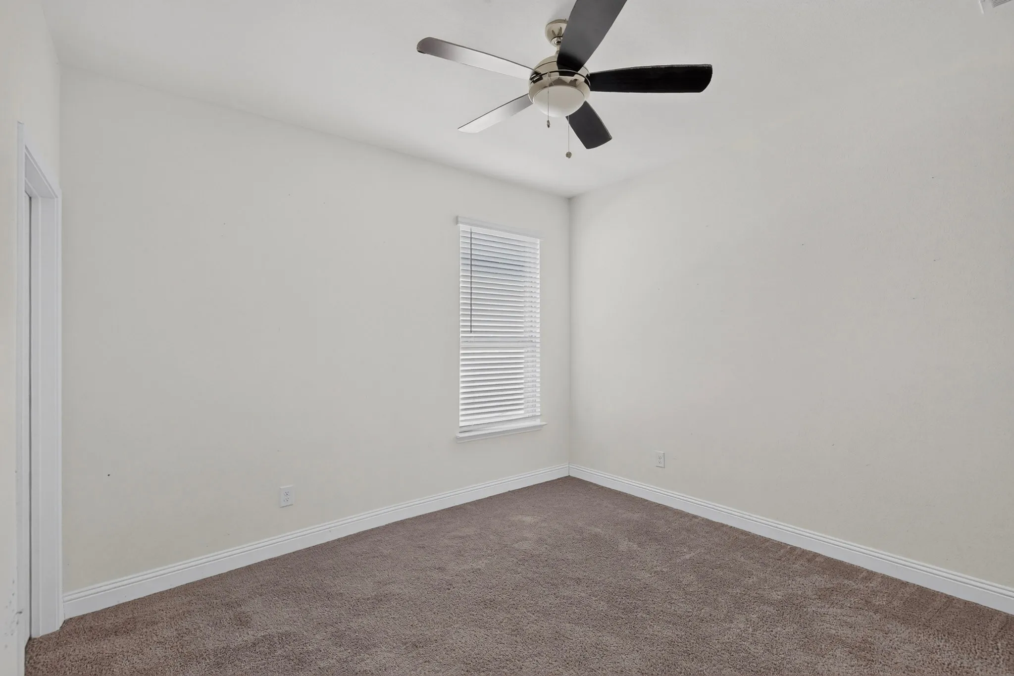 Neutral wall paint, brown carpet flooring, window with horizontal blinds, and a ceiling fan with integrated lighting