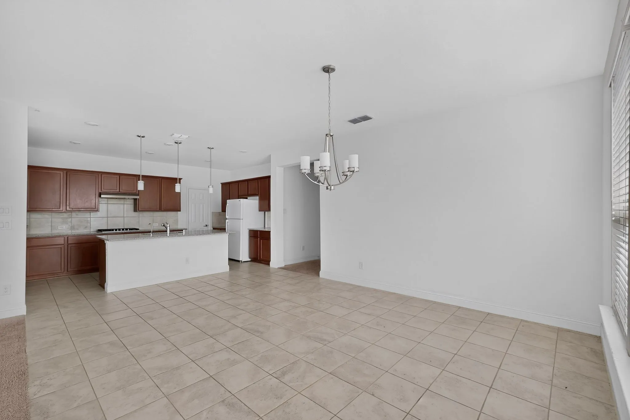 Kitchen featuring wood-finish cabinetry, granite countertops, tile backsplash, a gas range with a stainless steel hood, and a kitchen island with an integrated sink and pendant lighting