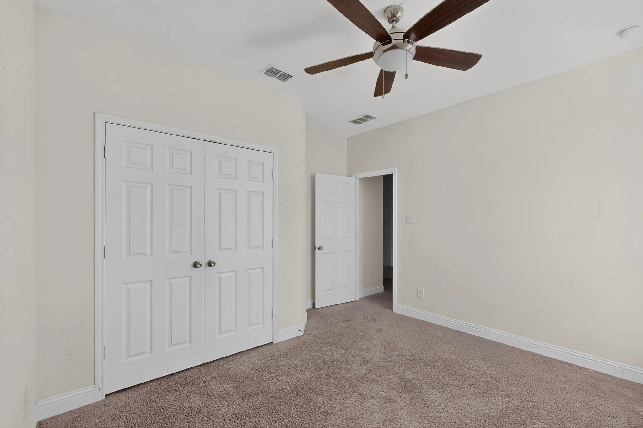 Neutral wall paint, brown carpeting, white baseboards, white panel doors, and ceiling fan with light fixture