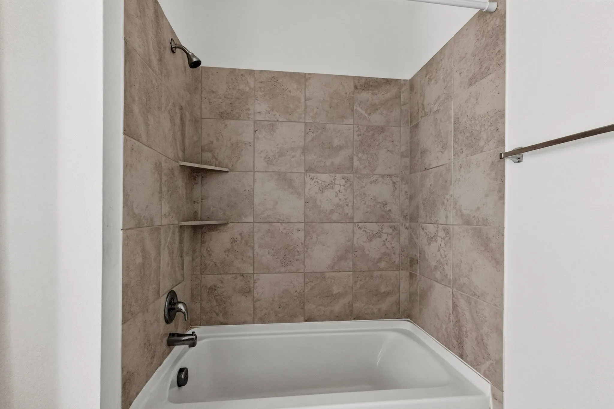 Bathtub with tiled surround, dual built-in shelving, and a dark bronze shower fixture