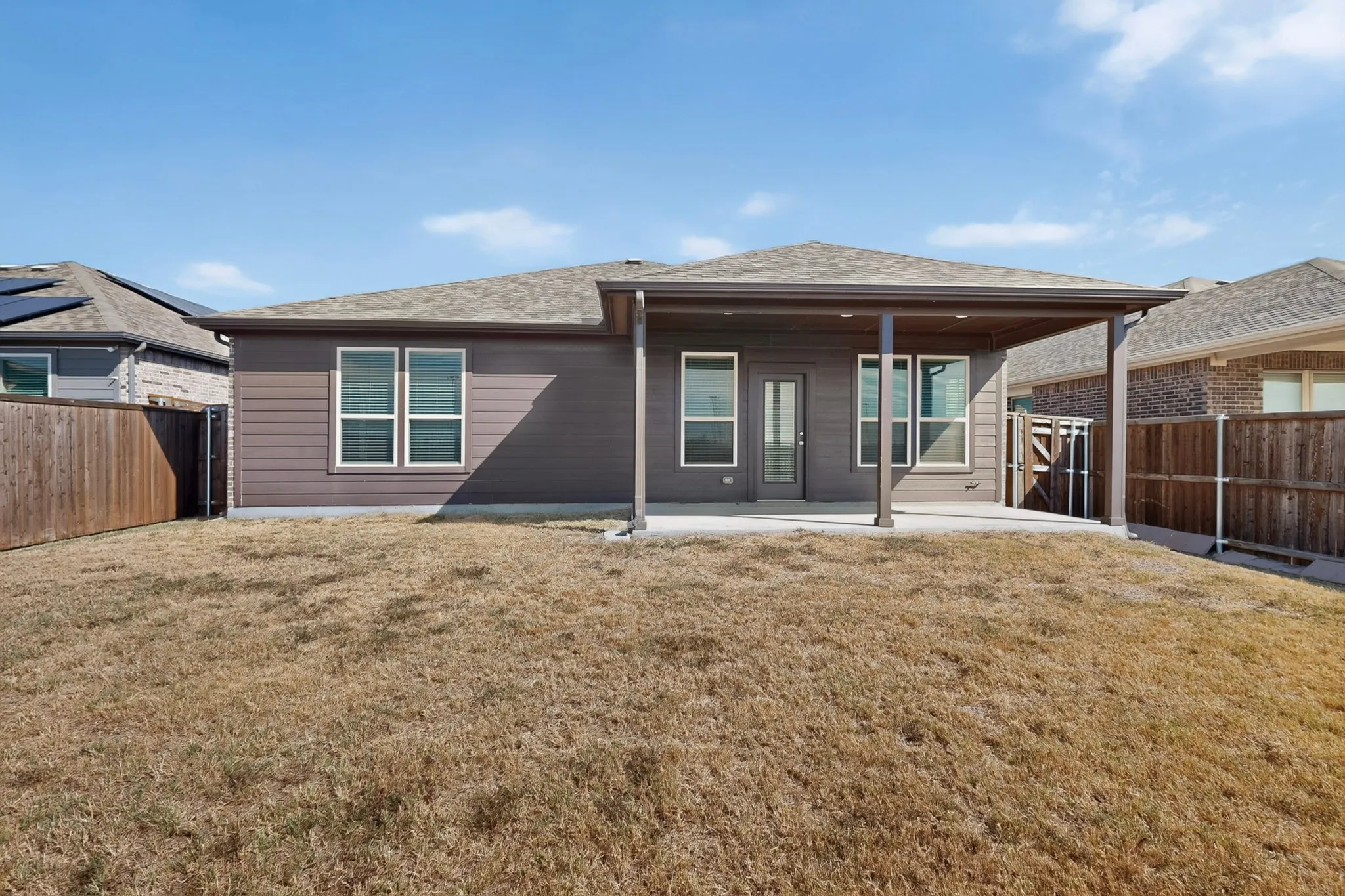 Rear exterior featuring a covered patio, multiple windows, and a privacy fence