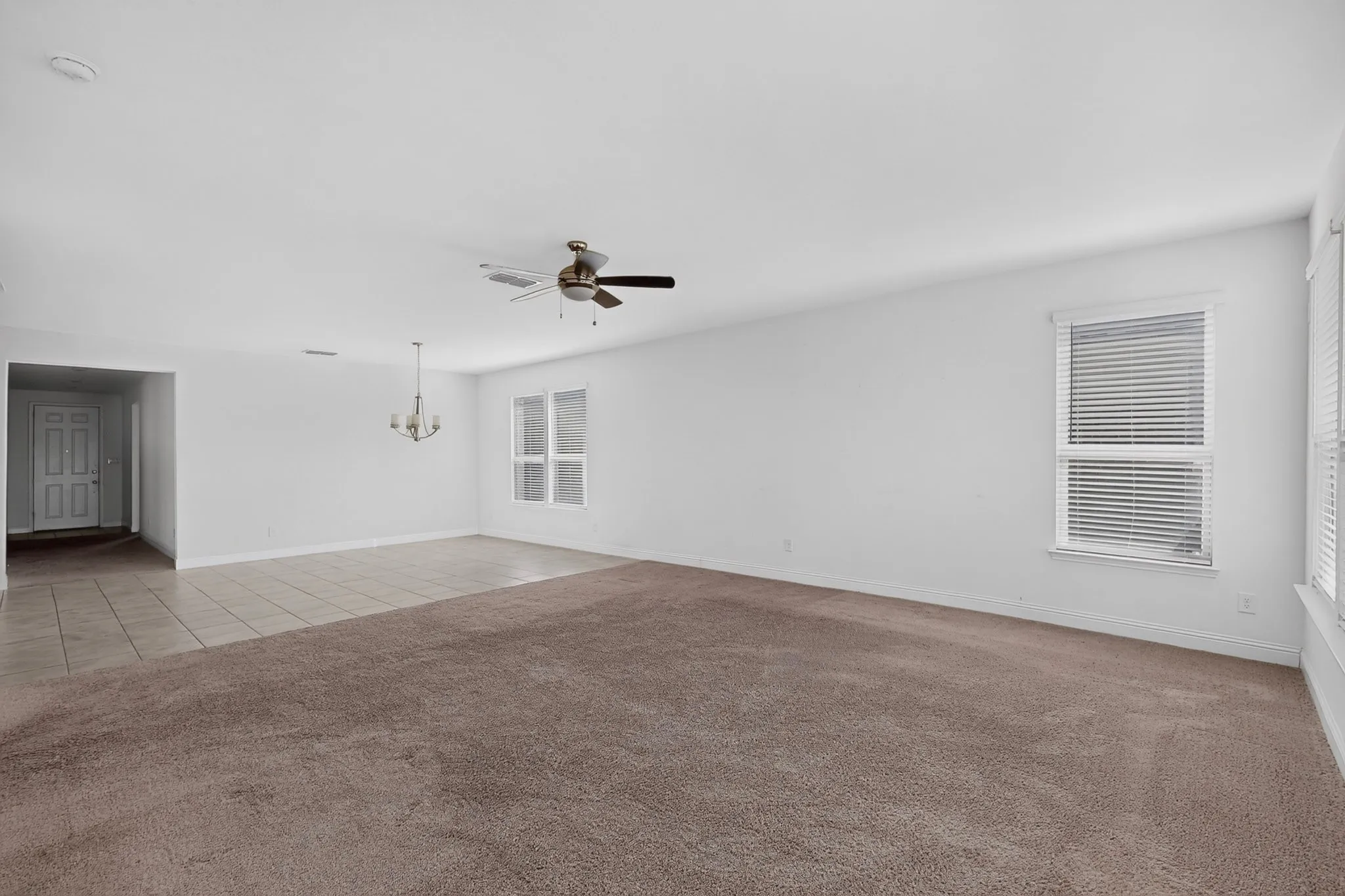 Spacious room featuring carpeting, tiled flooring, multiple windows, a ceiling fan, and a chandelier
