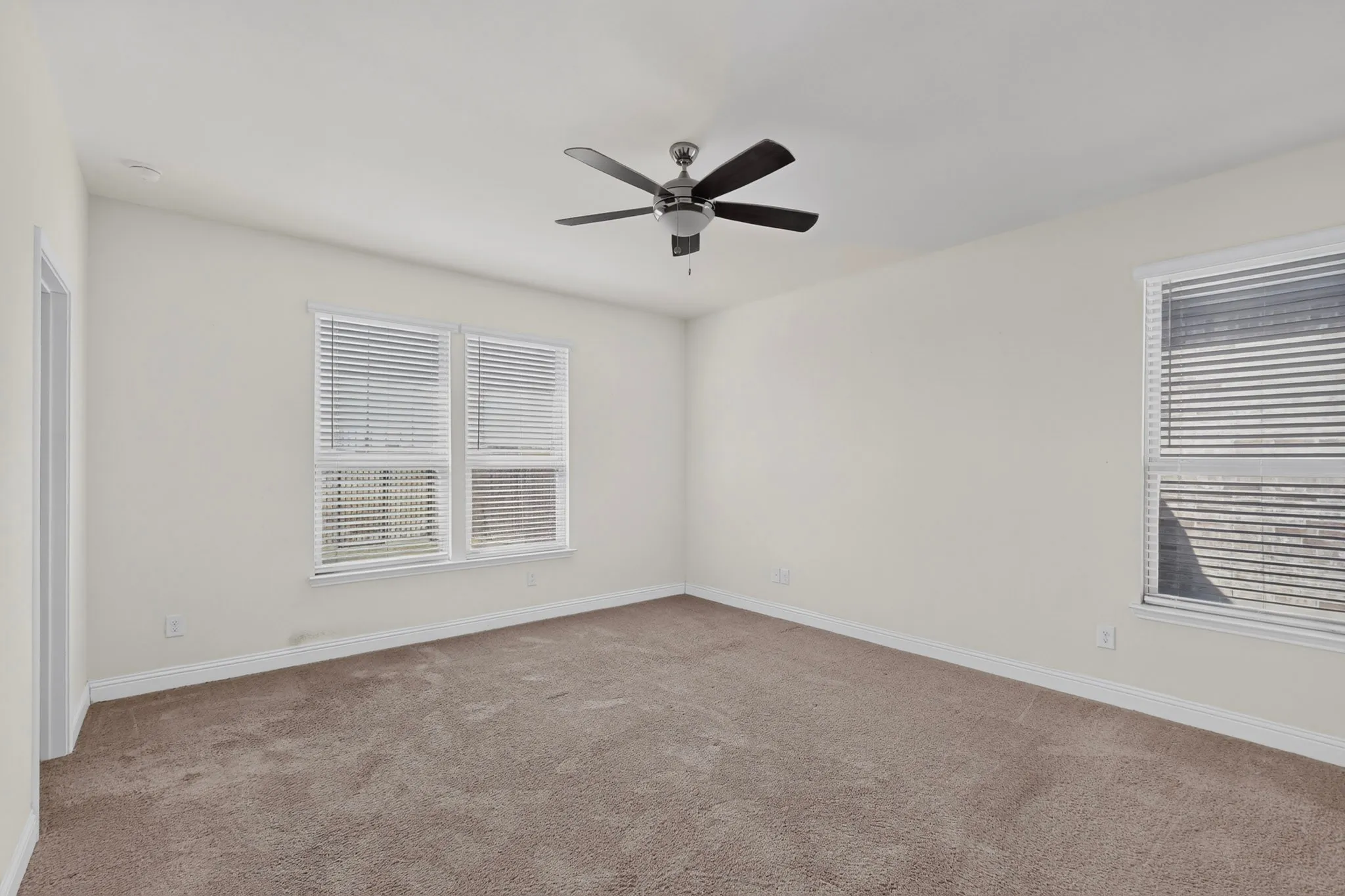 Carpeted room featuring a ceiling fan, multiple windows with blinds, and neutral wall tones