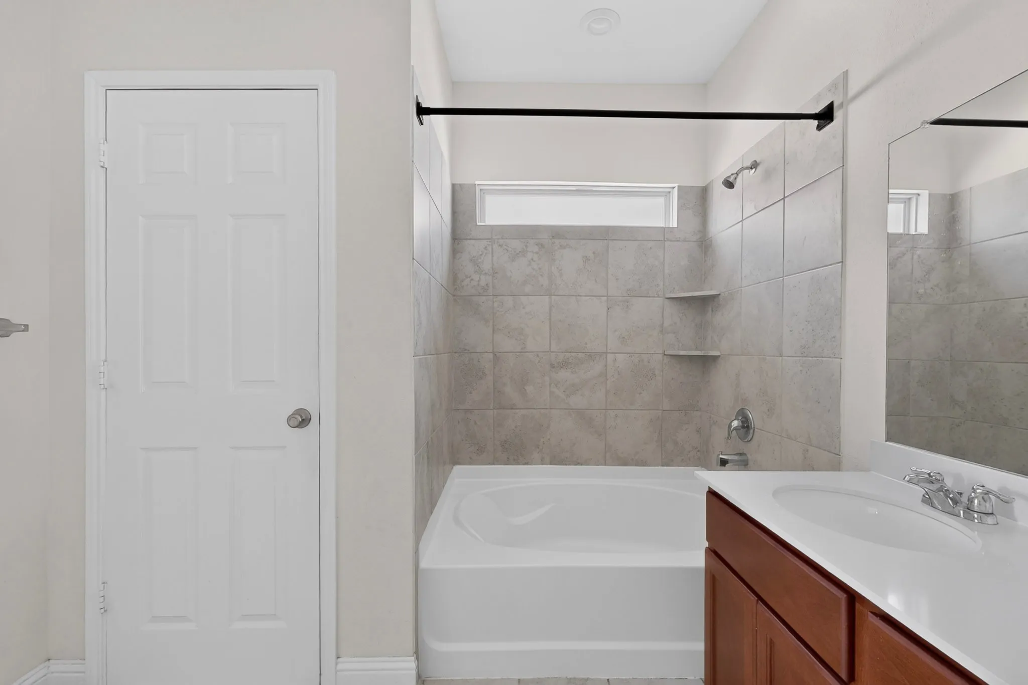 White paneled door, ceramic tile bath surround, built-in shower shelves, chrome plumbing fixtures, and a vanity with a white countertop