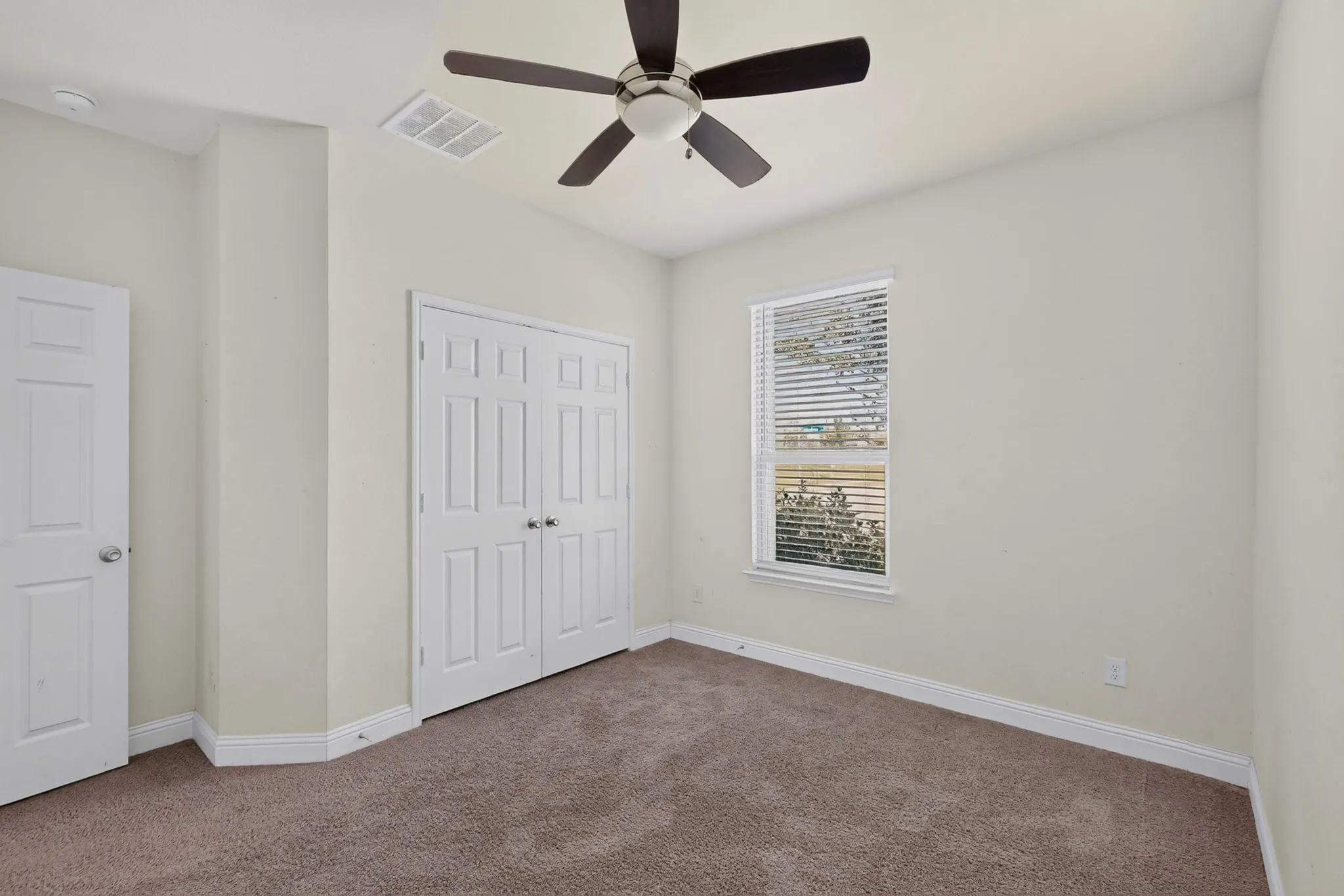 Neutral wall finishes, textured carpet, window with blinds, bi-fold closet doors, and a ceiling fan with integrated lighting