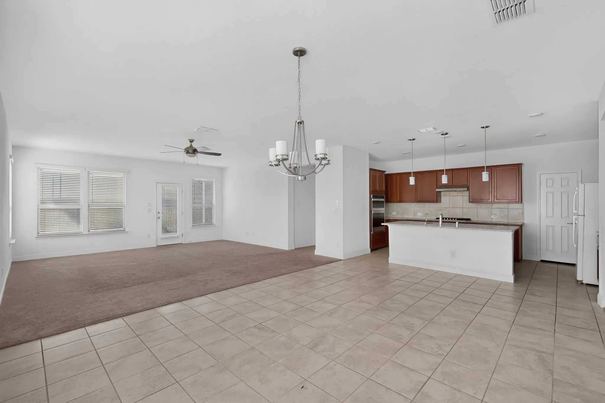 Spacious interior featuring a combination of carpet and tile flooring, kitchen with dark wood-finish cabinetry and light-colored countertops, island with integrated sink, and an overhead chandelier