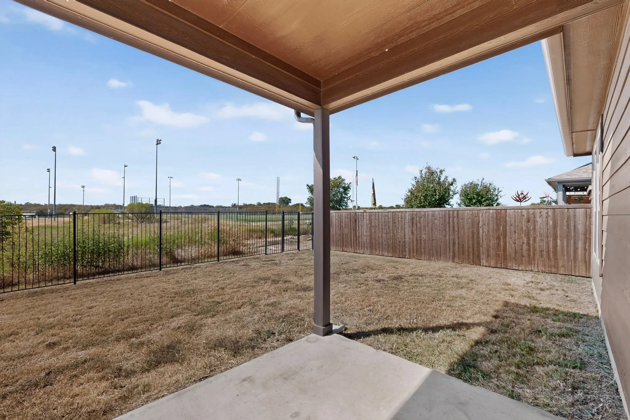 Concrete patio with an overhead cover, wood privacy fencing, and a black wrought iron fence