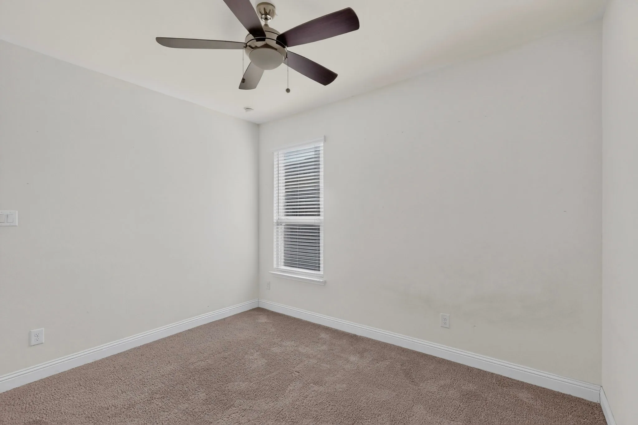 Carpeted flooring, white walls, single window with blinds, ceiling fan with light fixture