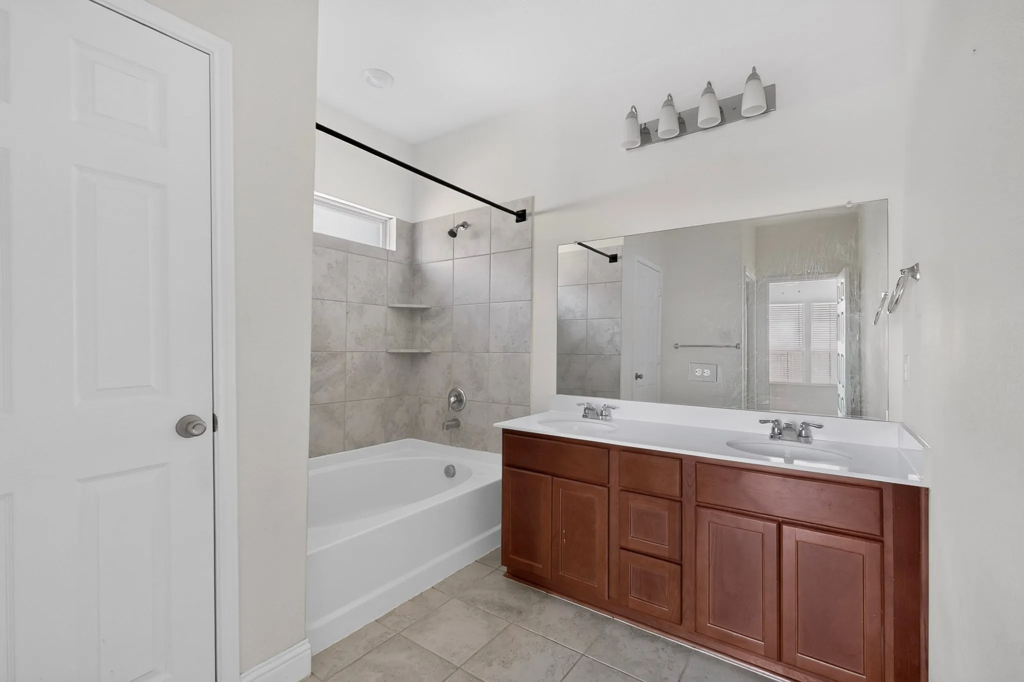 Dual-sink vanity with wood-finish cabinetry, a large mirror, and tiled flooring