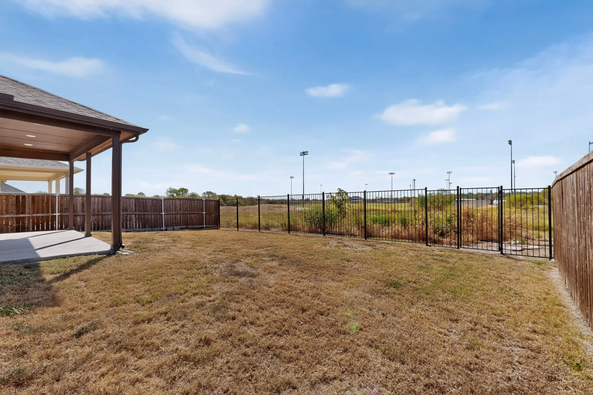 Covered patio with recessed lighting, concrete flooring, and an adjacent fenced yard featuring wood and black metal fencing