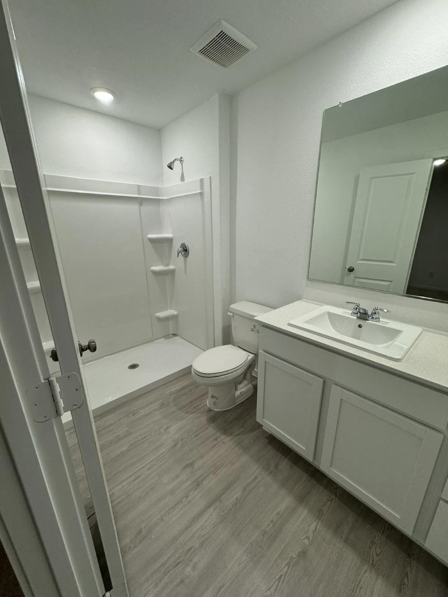 Bathroom featuring light wood-finish flooring, a white vanity with panel-front cabinetry, a white rectangular sink, and a shower with built-in shelving