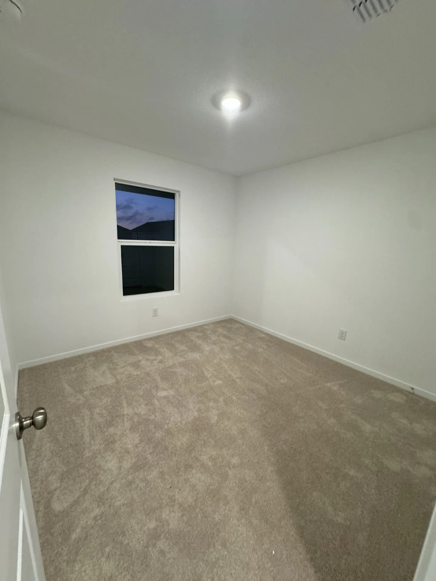 Recessed ceiling lighting, neutral tone carpeting, white painted walls, and a window with a dark frame