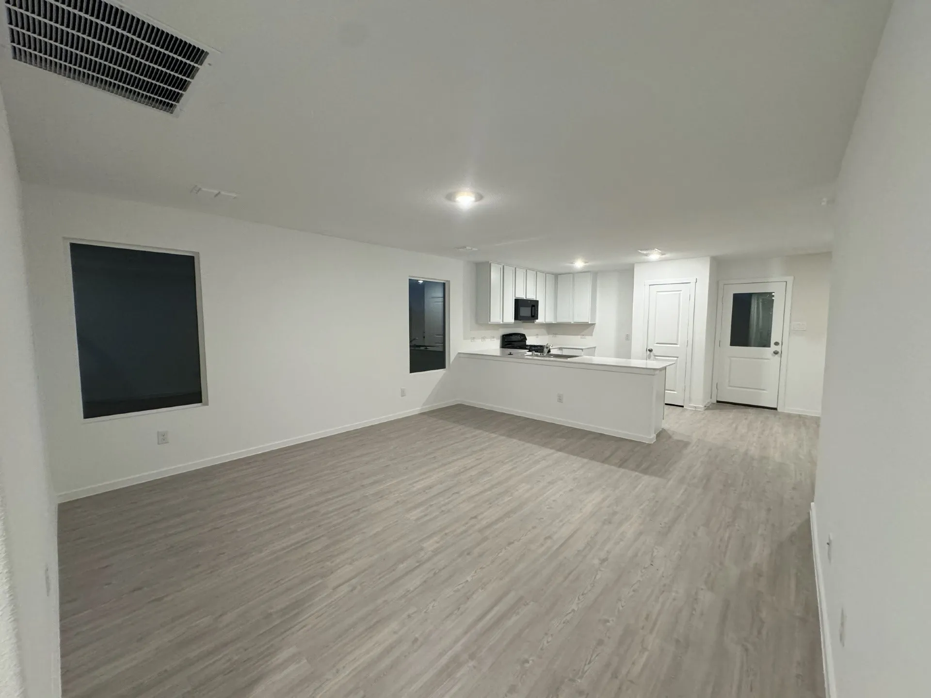 Open-concept living space featuring wood-finish flooring, recessed lighting, and a kitchen with white cabinetry and a built-in microwave