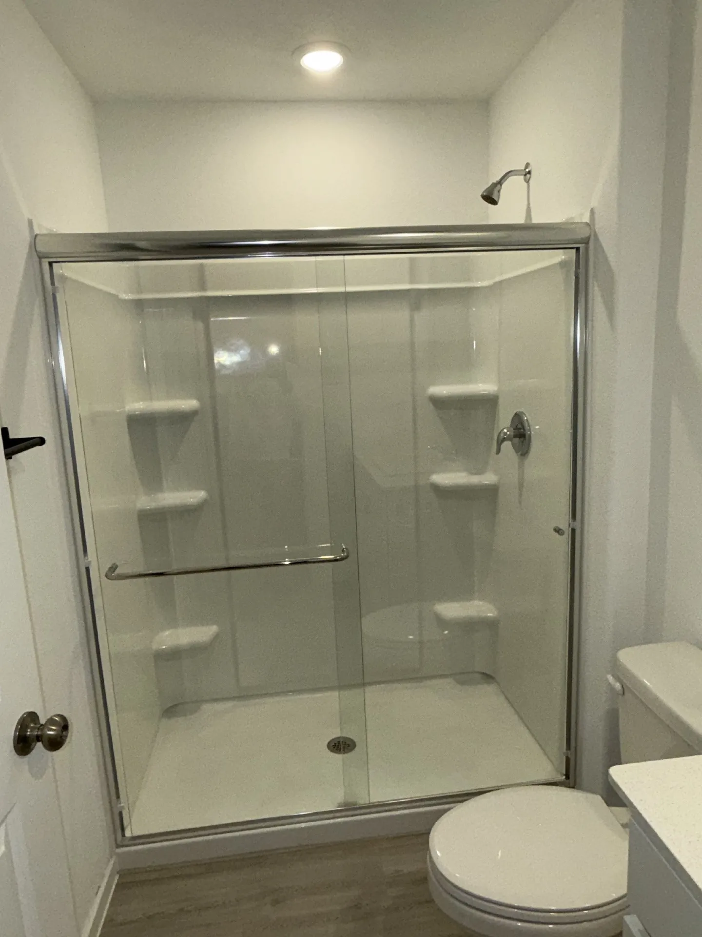 Shower enclosure with clear glass sliding doors and integrated shelving, featuring a chrome showerhead and faucet