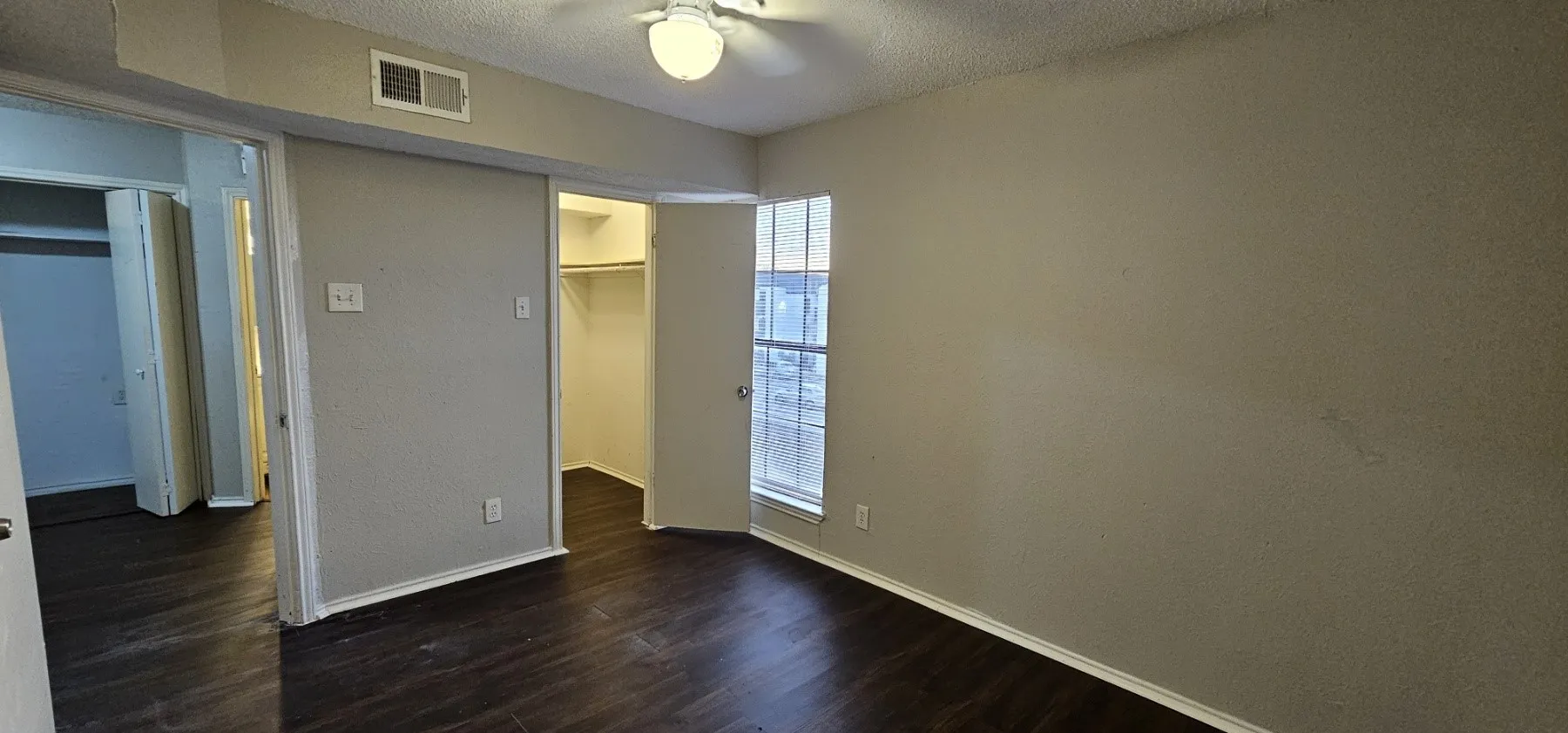 Dark wood-finish flooring, neutral wall tones, ceiling-mounted light fixture, white trim, and a window with blinds