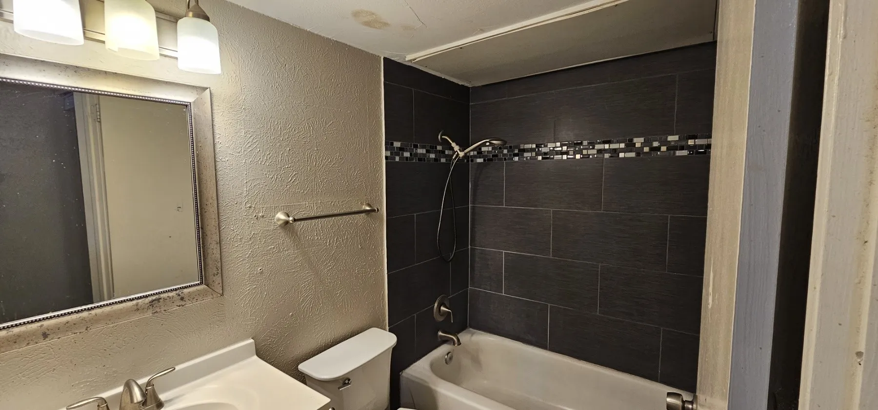 Ceramic tile shower surround with mosaic accent band, full bathtub, and vanity with integrated sink