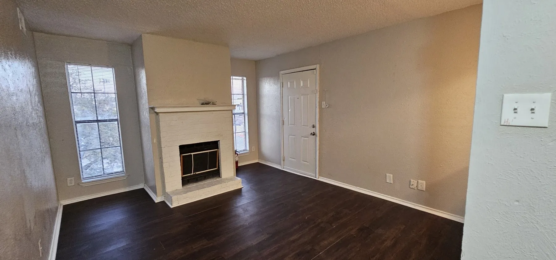 Living area featuring wood-finish flooring, a white brick fireplace with a mantel, and multiple windows