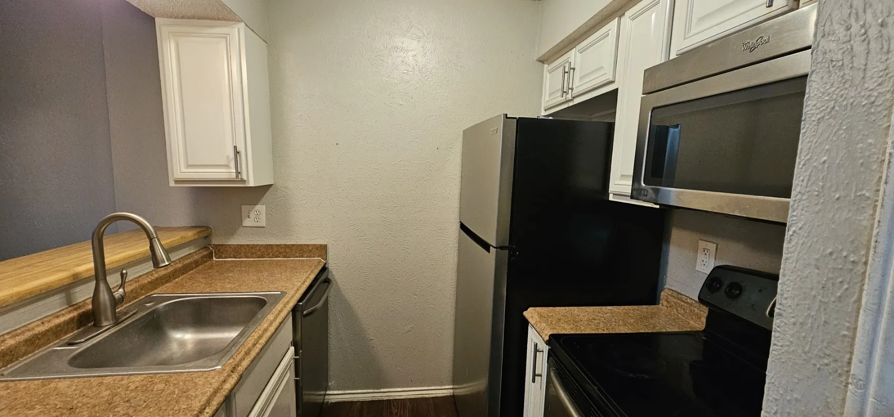 Kitchen featuring white cabinetry, wood-finish countertops, stainless steel sink with gooseneck faucet, black refrigerator, and stainless steel microwave