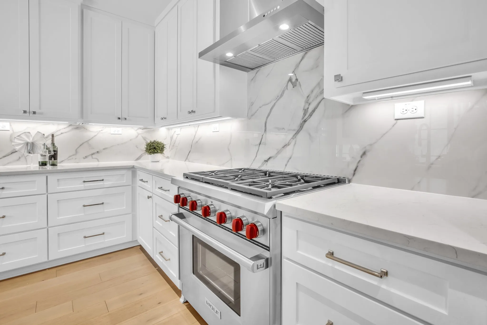 Kitchen with light stone countertops, luxury stove, ventilation hood, and white cabinetry