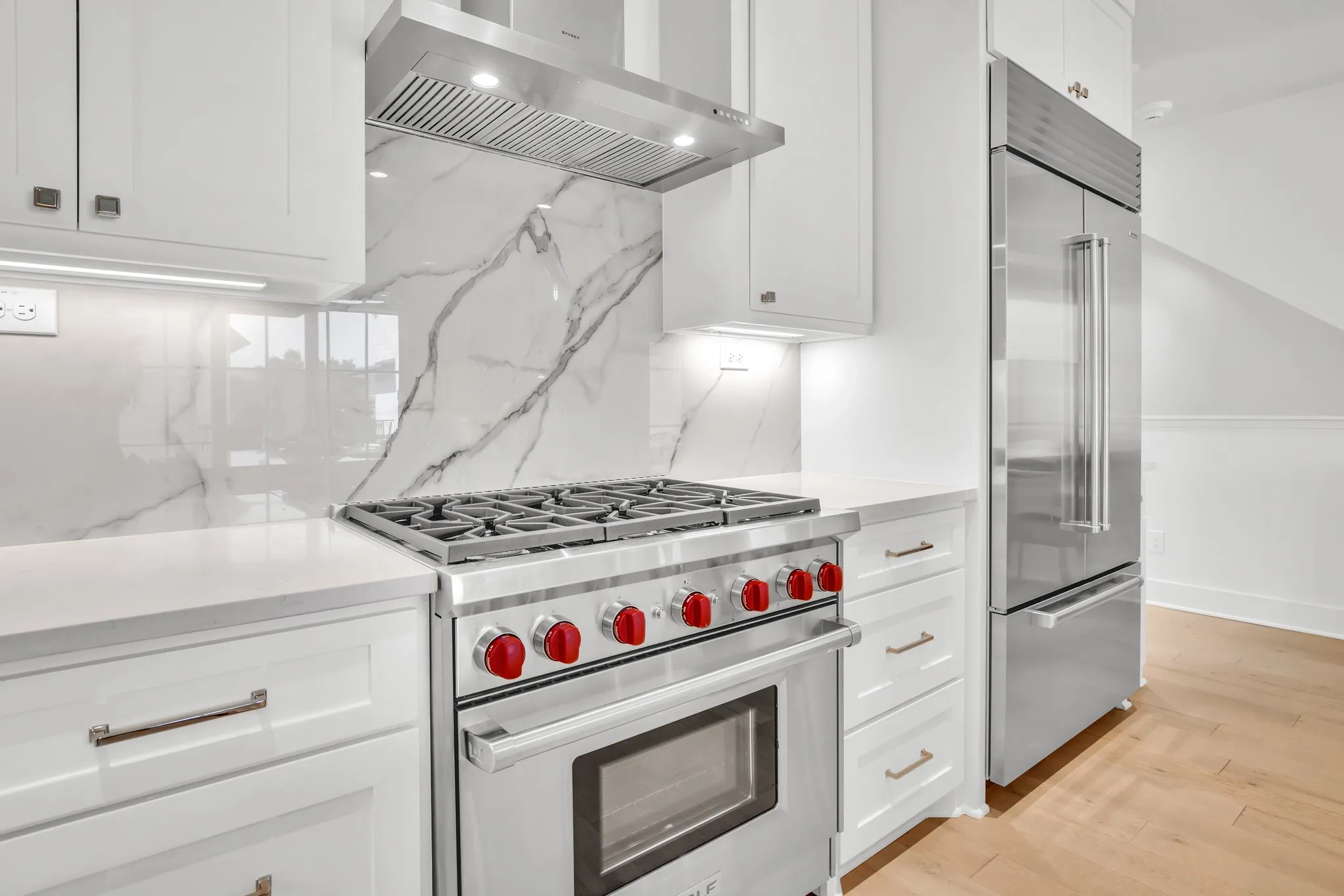 Kitchen with high quality appliances, ventilation hood, white cabinetry, light wood finished floors, and backsplash