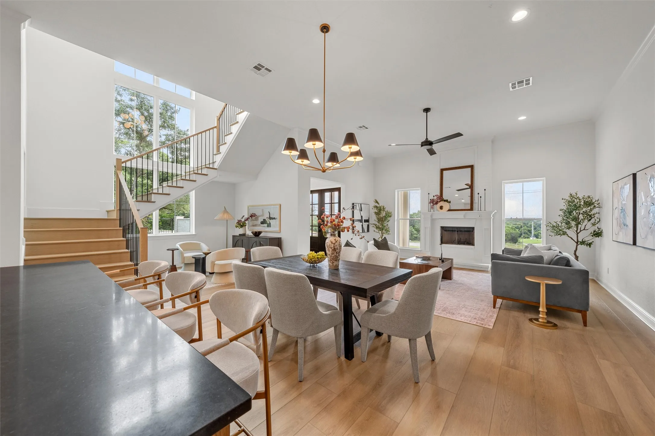 Open-concept living space with wood-finish flooring, a two-story ceiling, and a prominent fireplace with a decorative mantel