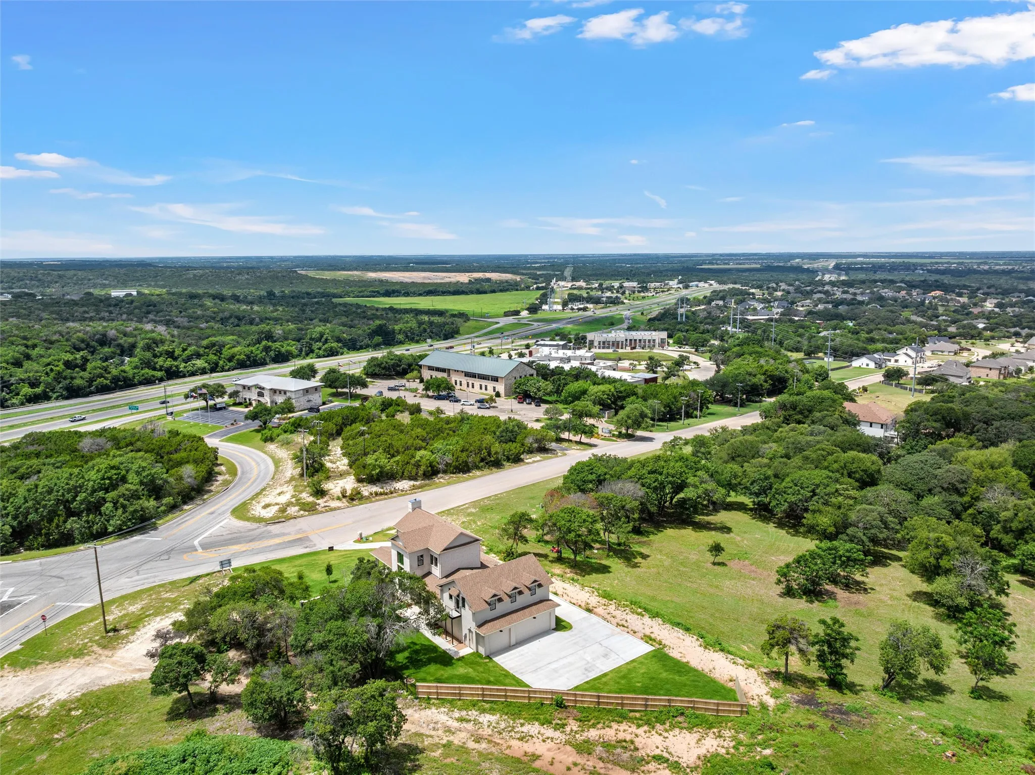 Aerial perspective showcasing a property with a light-colored exterior and multi-gabled roof, featuring a concrete driveway and a fenced perimeter