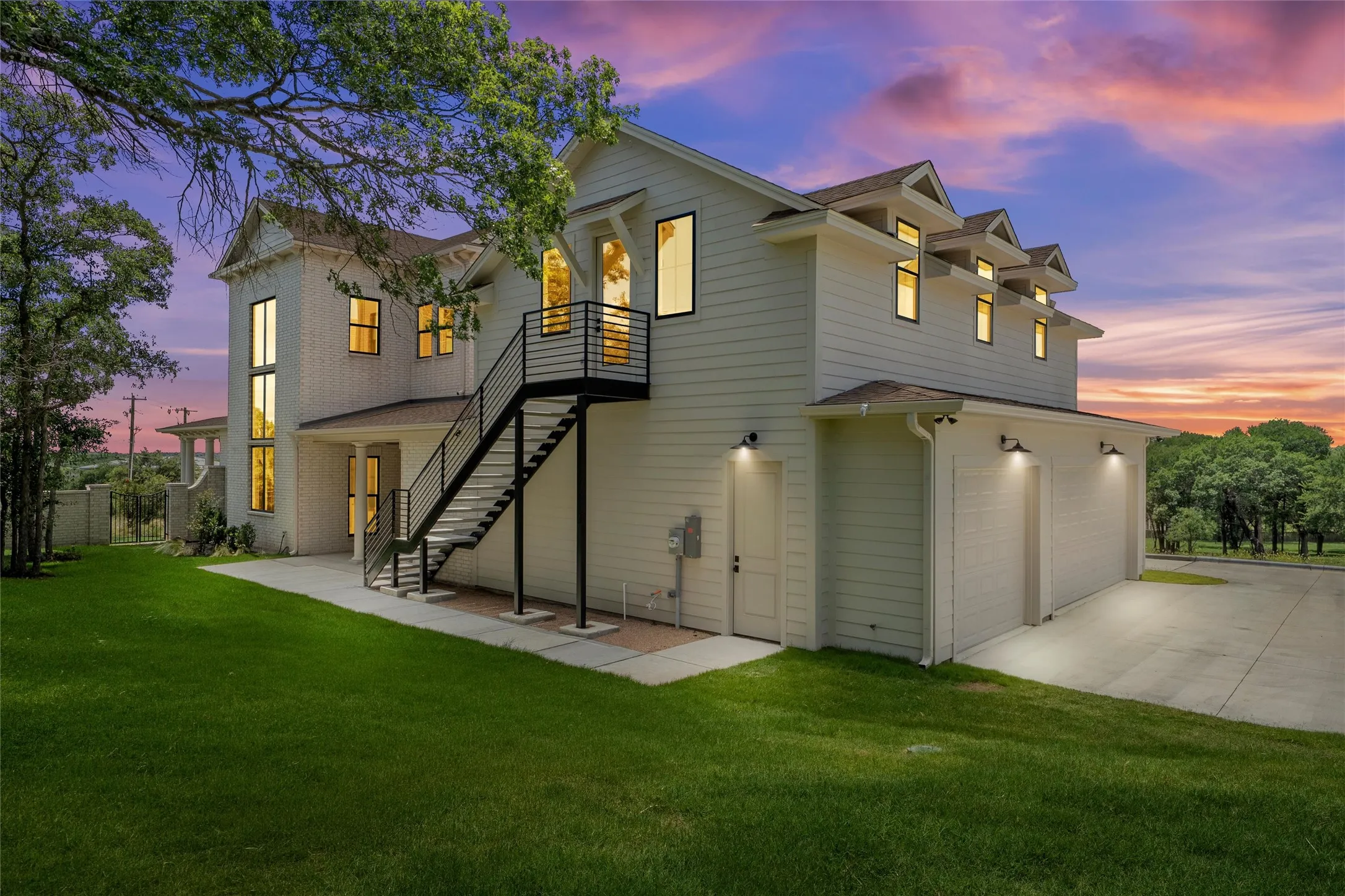 White siding exterior with multiple dormer windows, a three-car garage, and an external metal staircase with railing