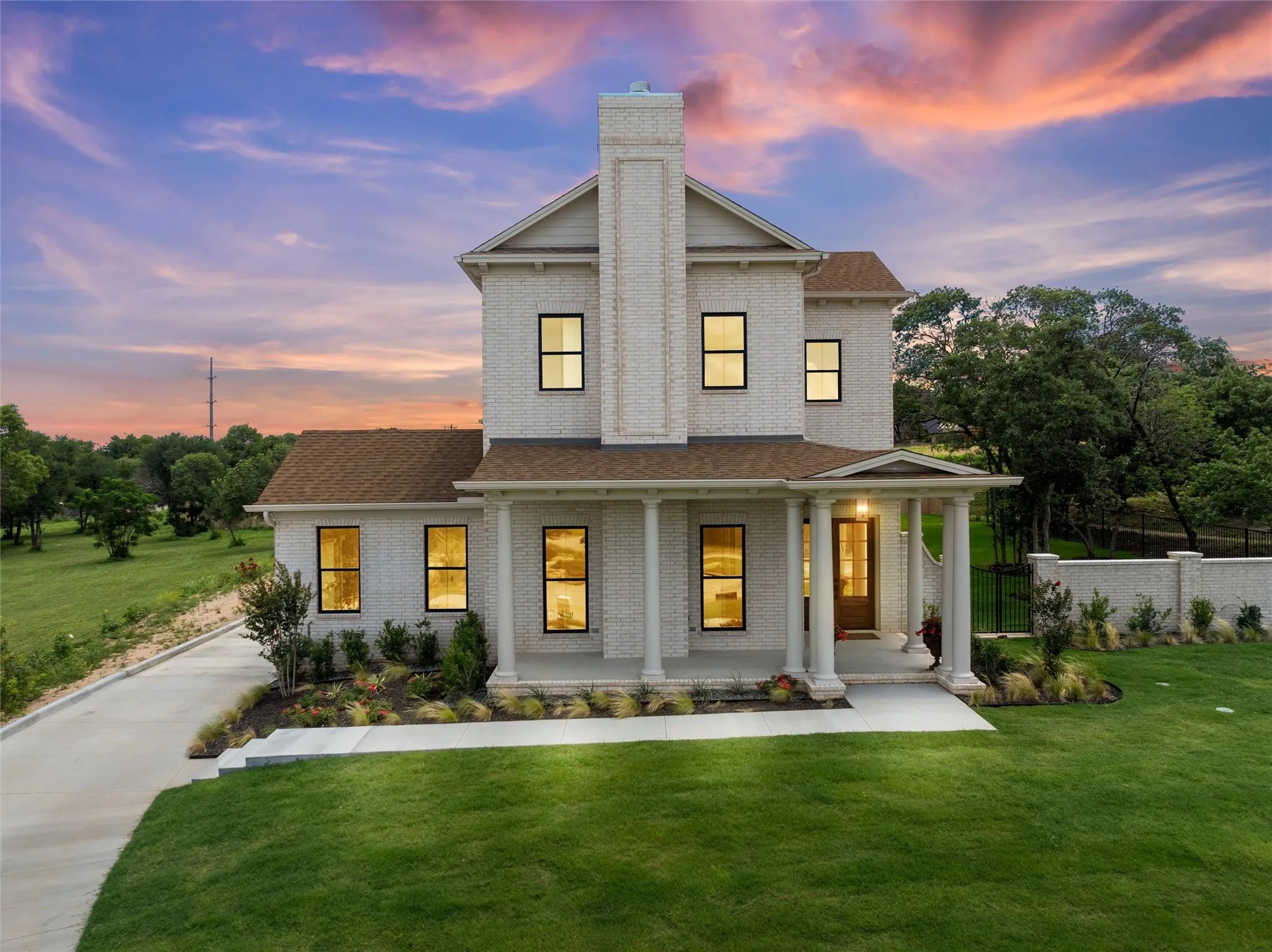 Two-story residence featuring a brick exterior, prominent chimney, covered front porch with columns, and a concrete driveway